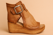 Tan leather wedge sandal with a distressed wood-texture platform, featuring a wide ankle wrap, large antique silver buckle, open toe, and natural creases in the soft leather upper.