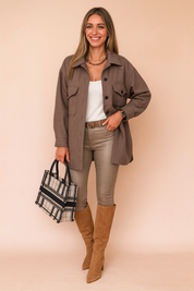 Taupe-brown button-up jacket with flap pockets and dark buttons, styled with a white top, slim beige pants, camel suede knee-high boots, and a plaid structured handbag.