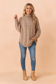 Taupe chunky knit turtleneck sweater with a central cable pattern, ribbed cuffs and hem, paired with distressed light blue skinny jeans and tan suede ankle boots.