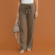 Taupe wide-leg drawstring linen pants with a relaxed fit, styled with a ribbed white tank top and beige thong sandals for a laid-back yet polished look.