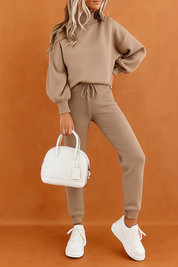 Relaxed taupe co-ord set with a balloon-sleeve pullover and high-waisted drawstring pants, styled with a structured white handbag and matching white platform sneakers.
