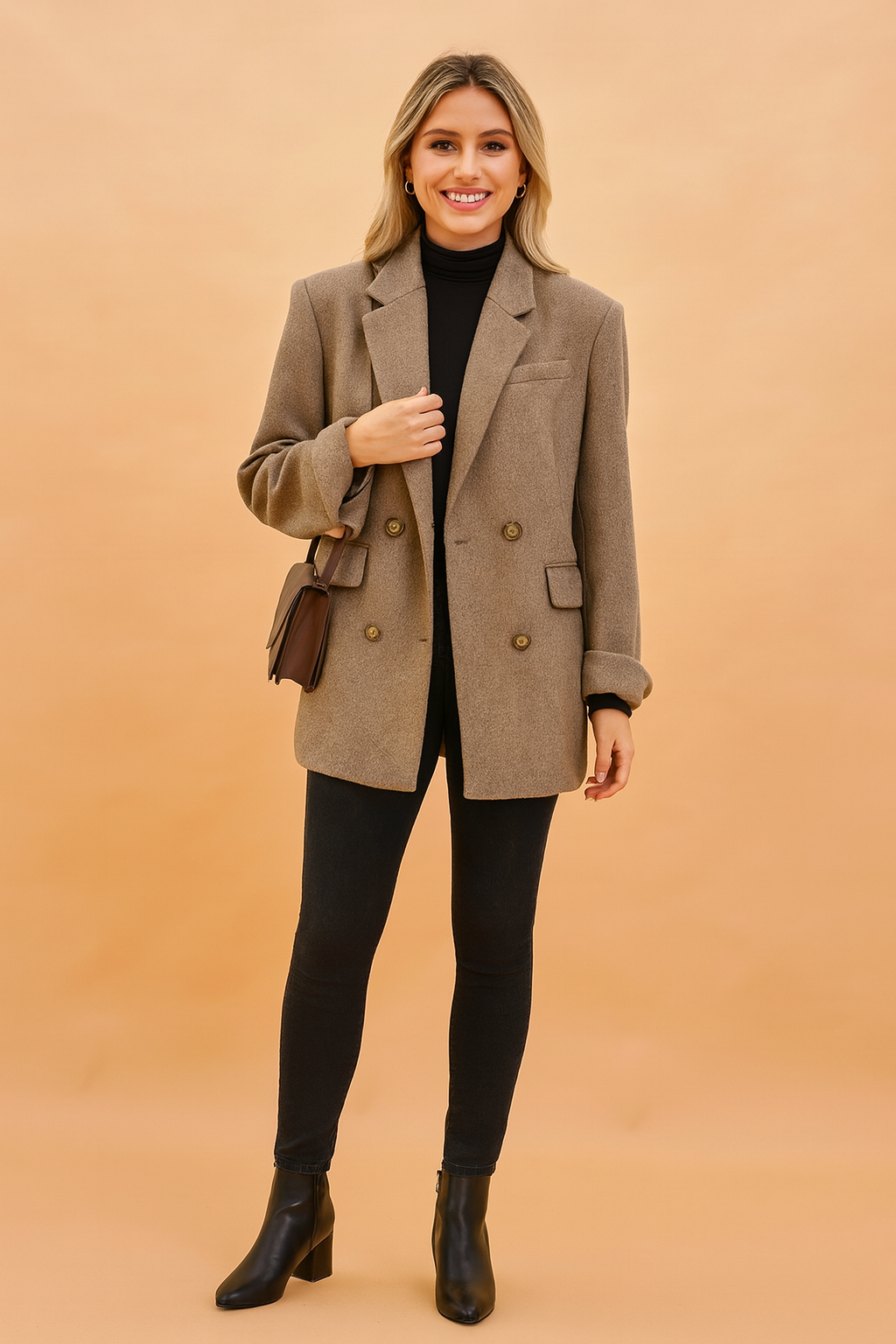 Taupe oversized wool blazer with double-breasted button closure, notch lapels, and flap pockets, styled over a black turtleneck top, paired with slim black jeans, black ankle boots, and a brown leather crossbody bag.