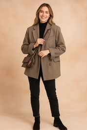 Taupe oversized wool blazer with double-breasted button closure, notch lapels, and flap pockets, styled over a black turtleneck top, paired with slim black jeans, black ankle boots, and a brown leather crossbody bag.
