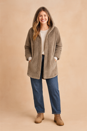 Taupe quilted long winter jacket with hood, button-down front, and side pockets, styled with a white inner top and straight-leg blue jeans paired with beige suede boots.