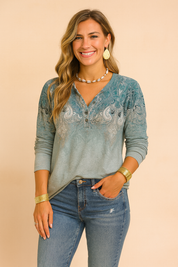 Elegant long-sleeve blouse featuring a teal and grey ornate paisley pattern, buttoned neckline, and soft gradient fabric with a relaxed fit.