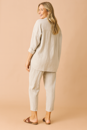 Loose-fit two-piece loungewear set featuring a textured beige weave, composed of a long-sleeved, drop-shoulder button-down top with a curved hem and matching tapered ankle-length pants with subtle vertical creasing for added structure.