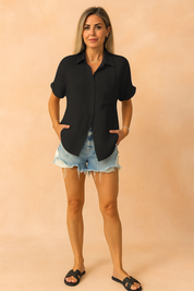 black button-up shirt with textured vertical pleats, styled with rolled sleeves and a chest pocket, paired with distressed denim shorts and white sneakers—perfect for casual summer looks.
