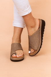 Textured taupe open-toe slide sandals featuring a wide asymmetrical upper with a subtle crosshatch linen-like pattern, raised platform sole in layered tan and black, and deep tread grip for added traction.
