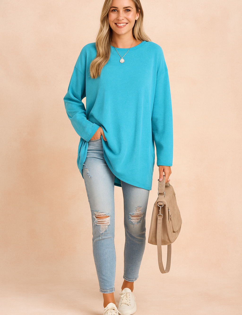 Long-sleeve oversized turquoise top with a relaxed fit, paired with light-wash distressed skinny jeans and casual white sneakers, styled with a taupe handbag.