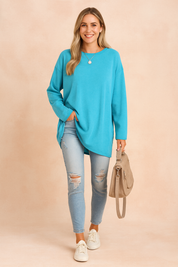 Long-sleeve oversized turquoise top with a relaxed fit, paired with light-wash distressed skinny jeans and casual white sneakers, styled with a taupe handbag.
