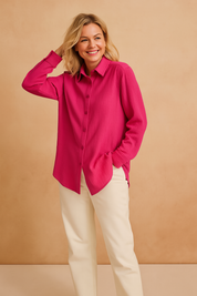 Vibrant hot pink textured button-up shirt with long sleeves, classic collar, and a relaxed hem, paired with high-waisted cream trousers.