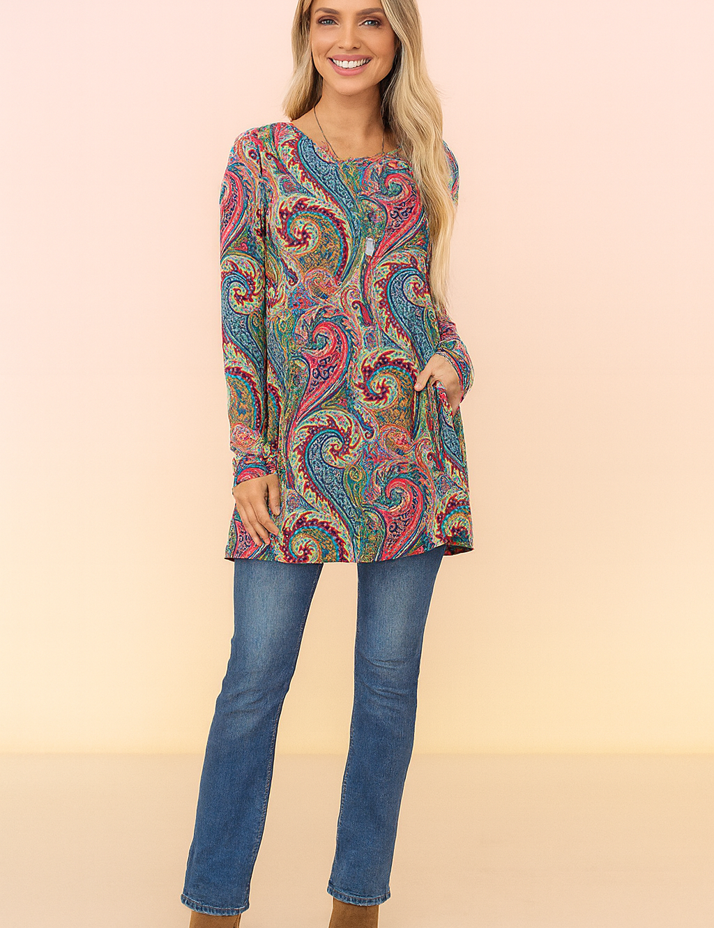 Long-sleeve tunic with vibrant paisley print in red, blue, green, and yellow, paired with blue straight-leg jeans and tan ankle boots.