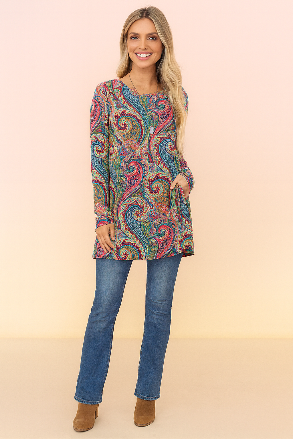 Long-sleeve tunic with vibrant paisley print in red, blue, green, and yellow, paired with blue straight-leg jeans and tan ankle boots.