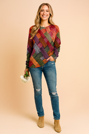 Colorful patchwork-print long-sleeve pullover sweater with a diamond pattern in red, orange, yellow, pink, and brown tones, paired with distressed blue jeans.