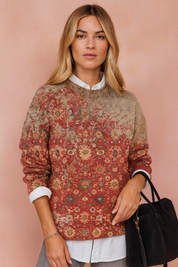  Vintage-inspired crewneck sweater with a faded red floral tapestry pattern, paired with a white button-up shirt layered underneath and accessorized with a black suede handbag.