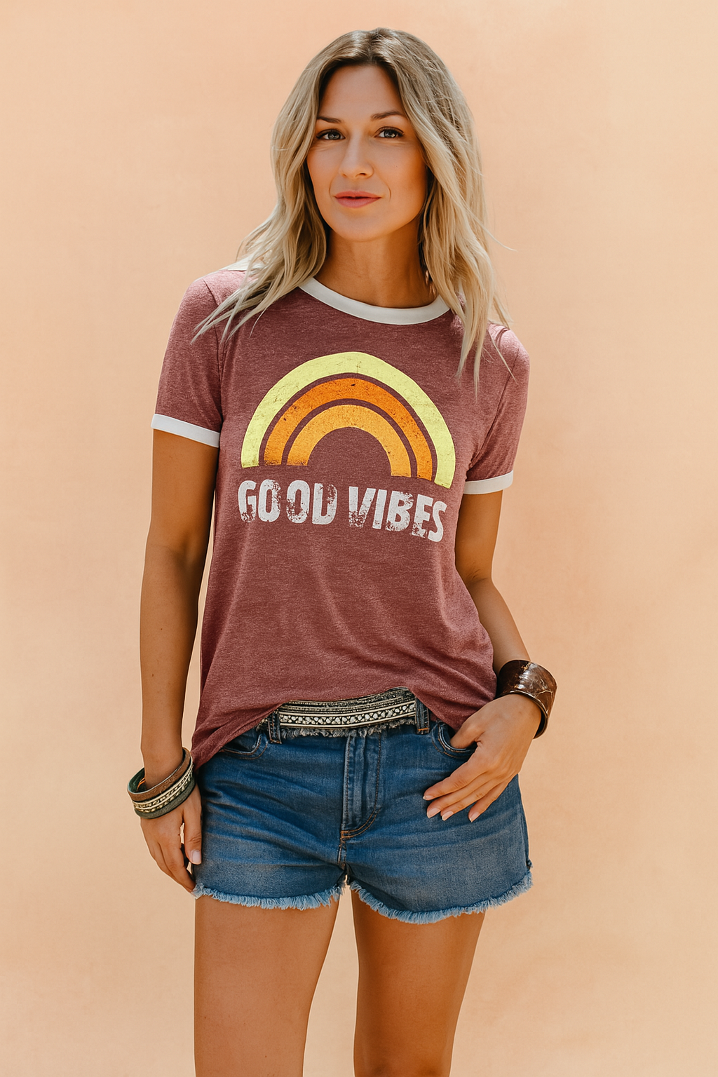 Vintage-style burgundy t-shirt with a retro rainbow graphic and distressed “Good Vibes” text, paired with casual denim shorts and boho accessories, ideal for laid-back summer fashion.