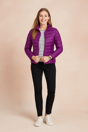 Violet quilted puffer jacket with horizontal stitching, high collar, and zip closure, styled with a striped shirt, slim black pants, and white shoe flats.