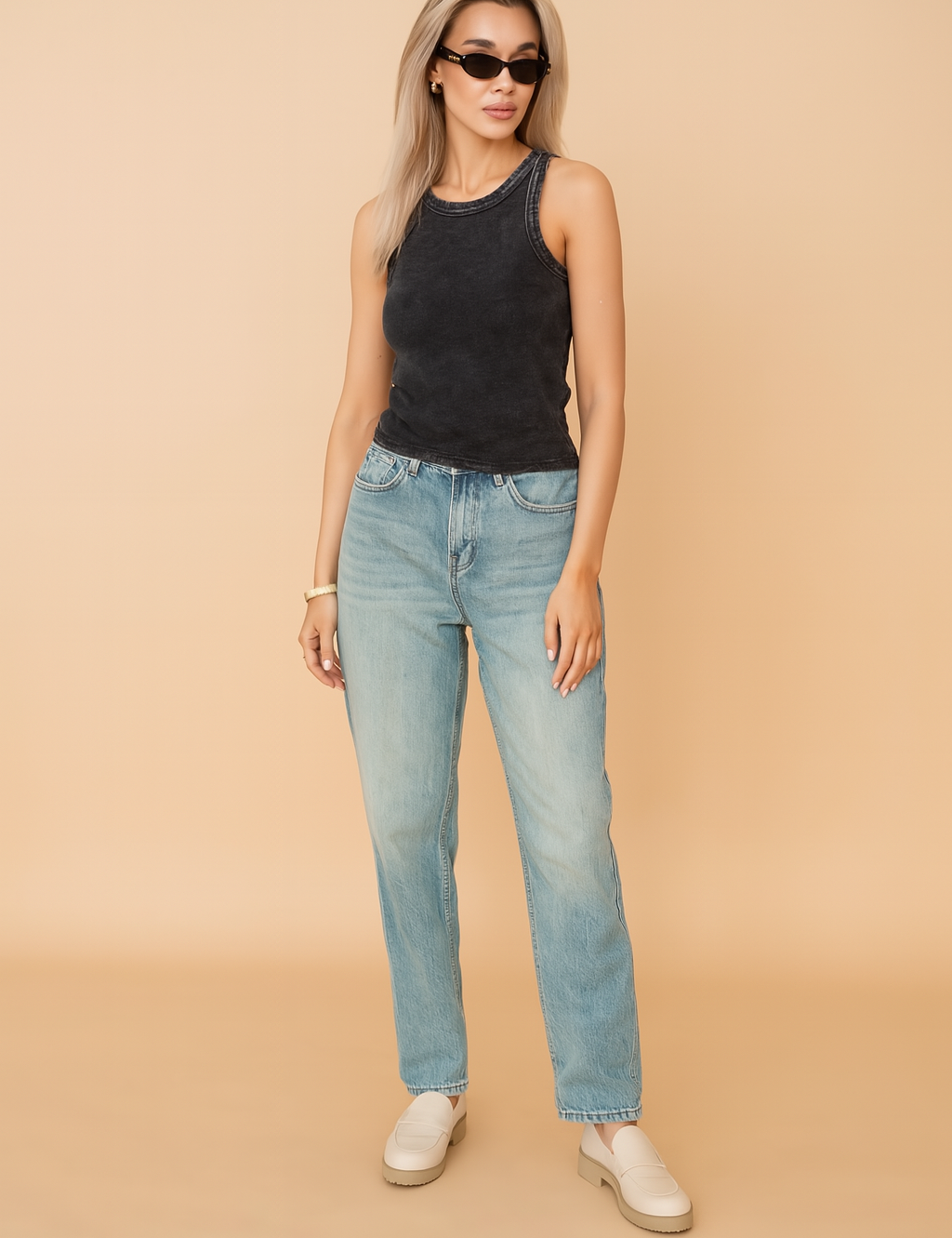 A stylish sleeveless washed black tank top with a faded finish, paired with high-waisted light blue denim jeans featuring a slight front rip. The outfit highlights a modern casual look ideal for everyday wear, with emphasis on texture and fit