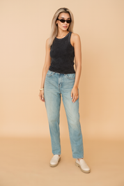 A stylish sleeveless washed black tank top with a faded finish, paired with high-waisted light blue denim jeans featuring a slight front rip. The outfit highlights a modern casual look ideal for everyday wear, with emphasis on texture and fit
