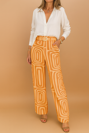 White button-up blouse paired with high-waisted wide-leg orange pants featuring a bold geometric print and matching fabric belt, styled with open-toe heels.