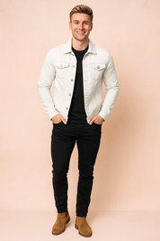 White denim jacket with button closure, twin flap chest pockets, and tailored seams, styled over a black t-shirt with slim black pants and tan suede Chelsea boots for a sharp casual look.