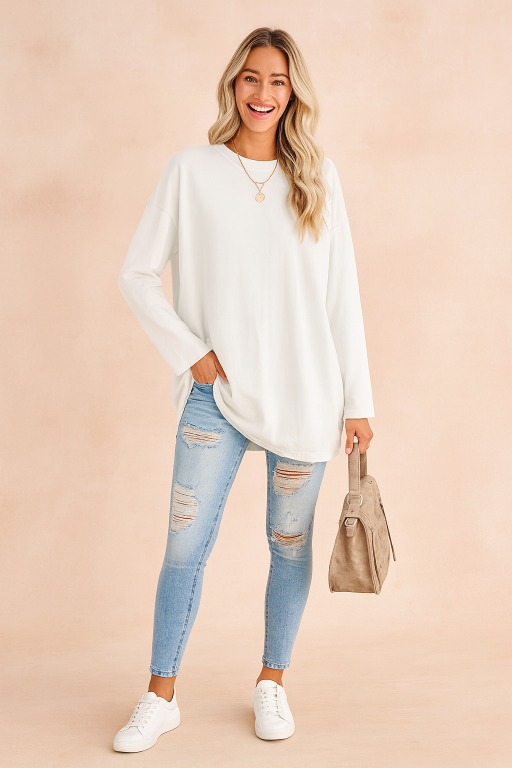 White oversized long-sleeve sweatshirt paired with light-wash distressed skinny jeans, complemented by white sneakers, a taupe handbag, and a gold pendant necklace.