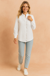 Textured white button-up blouse with a ruffled stand collar and concealed placket, paired with light-wash slim jeans and white sneakers.