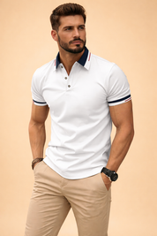Slim-fit white short-sleeve polo shirt with navy contrast collar and sleeve cuffs, subtle red stripe detailing, three-button placket, paired with tailored beige chinos for a clean smart-casual look.