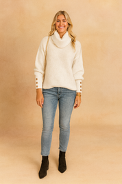 White ribbed turtleneck sweater with buttoned sleeve accents paired with light blue fitted jeans for a chic casual look.