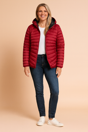 Lightweight quilted puffer jacket in deep wine red with horizontal stitching, front zipper closure, side zip pockets, and black inner lining, styled over a plain white top with dark blue slim-fit jeans and white sneakers.