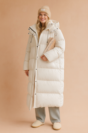 Women's long white puffer down jacket with hood, front button and zip closure, drawstring details, and oversized quilted design for winter wear