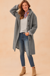 Women's long grey button-up wool coat with relaxed fit, paired with casual jeans and ankle boots, styled with a light grey V-neck top and a colorful neck scarf.