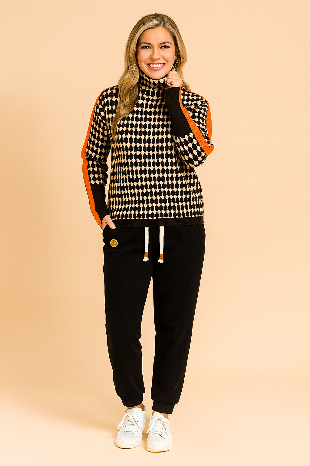 Oversized houndstooth turtleneck sweater with bold orange stripe detailing on sleeves, paired with black jogger pants and white sneakers.