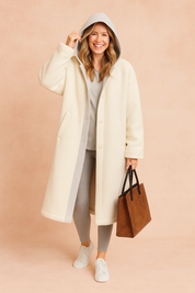 Long oversized hooded winter coat with button closure, inner contrast lining, and relaxed sleeves paired with jogger pants and sneakers.