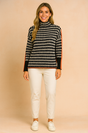 Oversized houndstooth turtleneck sweater with bold orange stripe detailing on sleeves, paired with black jogger pants and white sneakers.