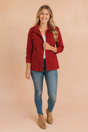 Women’s red casual utility jacket with front zipper, snap buttons, chest and side pockets, styled with jeans and ankle boots.