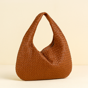 Cognac brown woven leather hobo bag with a relaxed silhouette and broad single strap, displayed on a minimalist beige background to emphasize the detailed basketweave texture.