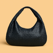 Navy blue woven leather hobo bag with a braided top handle and slouchy crescent silhouette, set against a beige background for a refined, artisanal look.