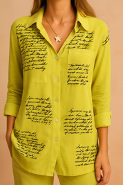 Lime green button-up blouse with black cursive script print, featuring a collared neckline, front patch pocket, and long sleeves, showcased in high-definition lighting that highlights the lightweight fabric and intricate text pattern design.