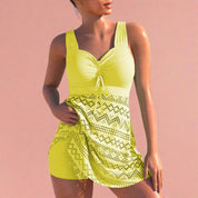 Stylish yellow swim dress featuring a ruched bust with central drawstring tie and wide shoulder straps, paired with a geometric mesh overlay skirt showcasing zigzag and diamond cut-out patterns in matching tones, layered over fitted shorts for a flattering beach-ready silhouette.