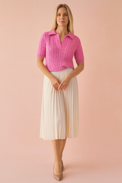 Bright pink cable-knit polo blouse with a collared neckline and short sleeves, paired with a high-waisted cream pleated midi skirt and beige heels.